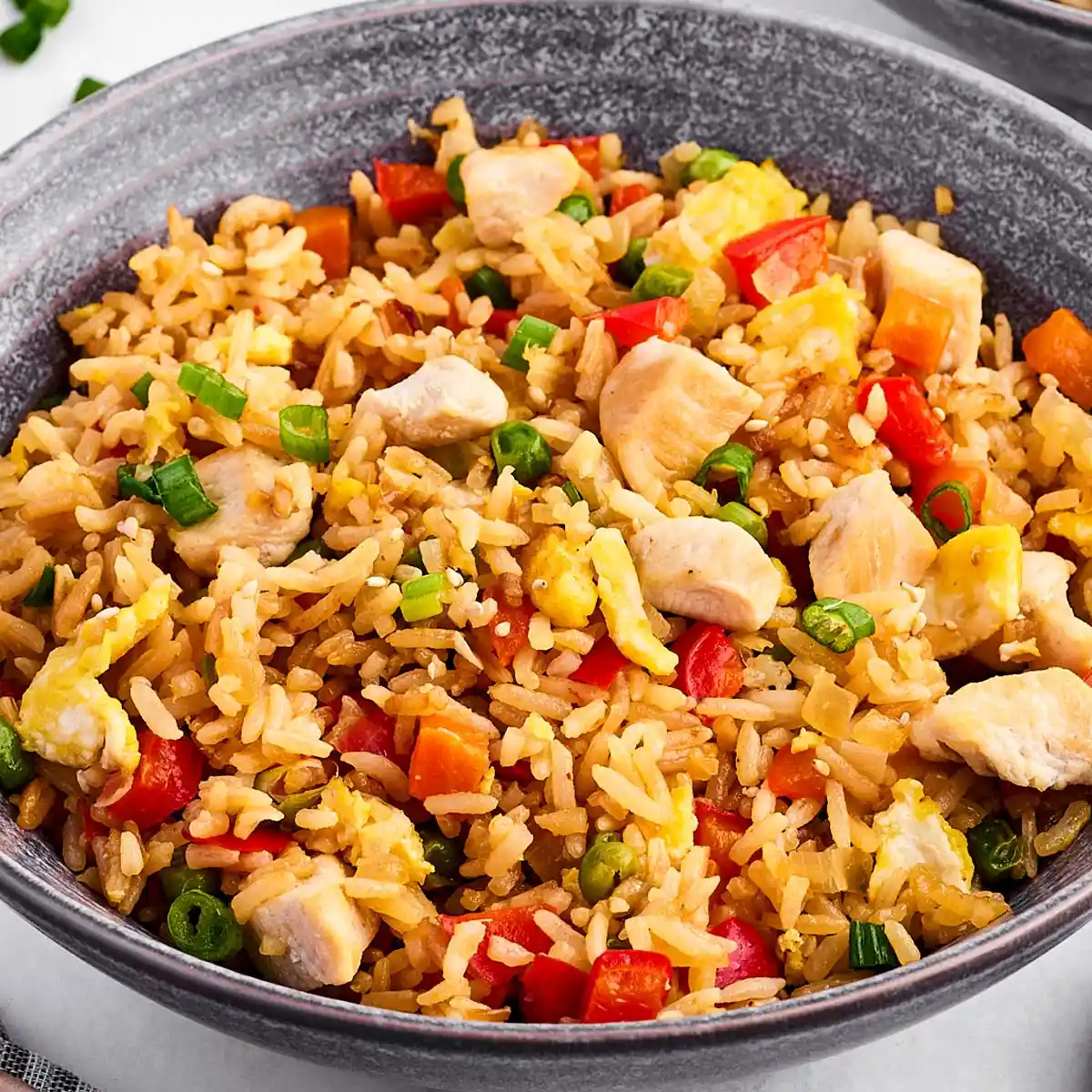 Easy Chicken Fried Rice Recipe 2 A large skillet containing homemade chicken fried rice with green onions and sesame seeds scattered on top