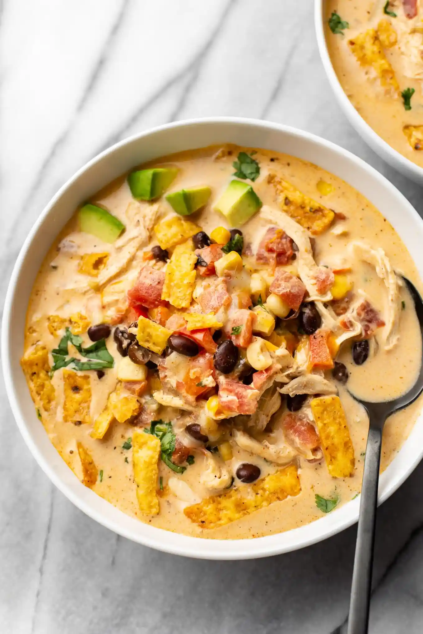 Easy Creamy Chicken Taco Soup Recipe 2 A bowl of creamy chicken taco soup topped with shredded cheese, fresh avocado slices, and chopped cilantro